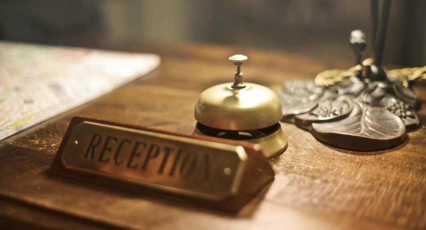 Old fashioned golden service bell and reception sign placed on wooden counter of hotel with retro interior